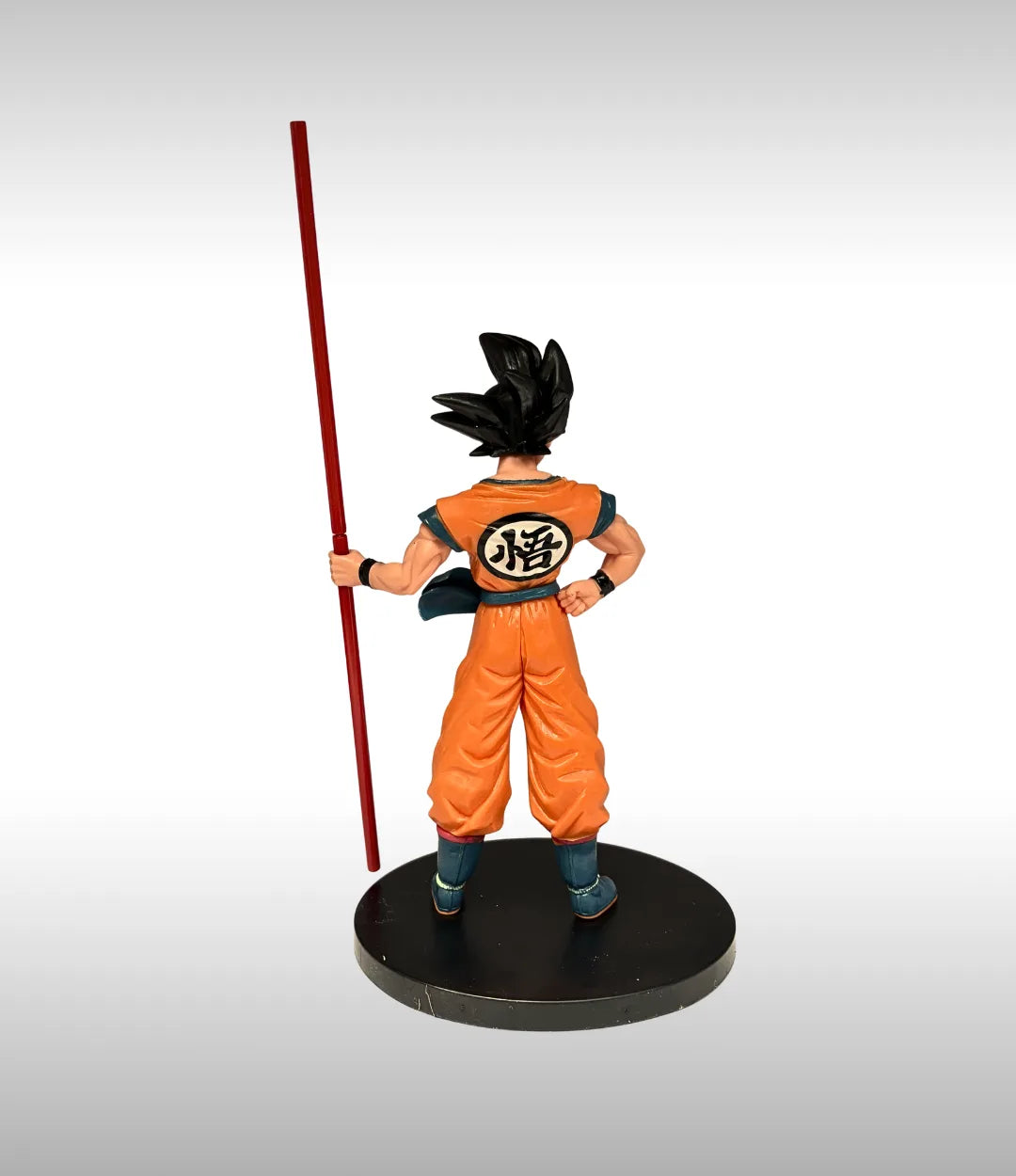 Figure of a character in an orange outfit with a red staff on a gray background
