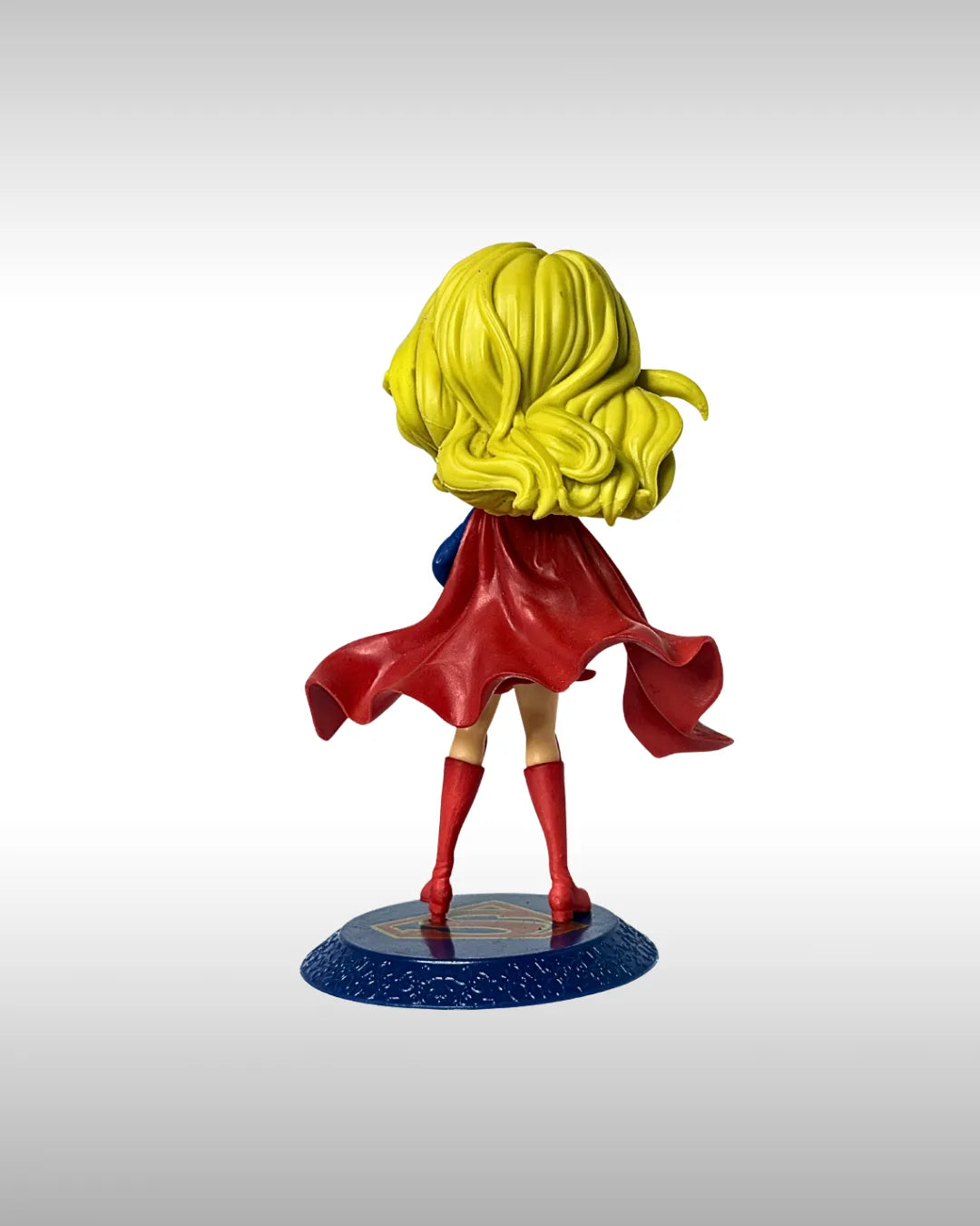 Superhero figurine with red cape and yellow hair on a gray background